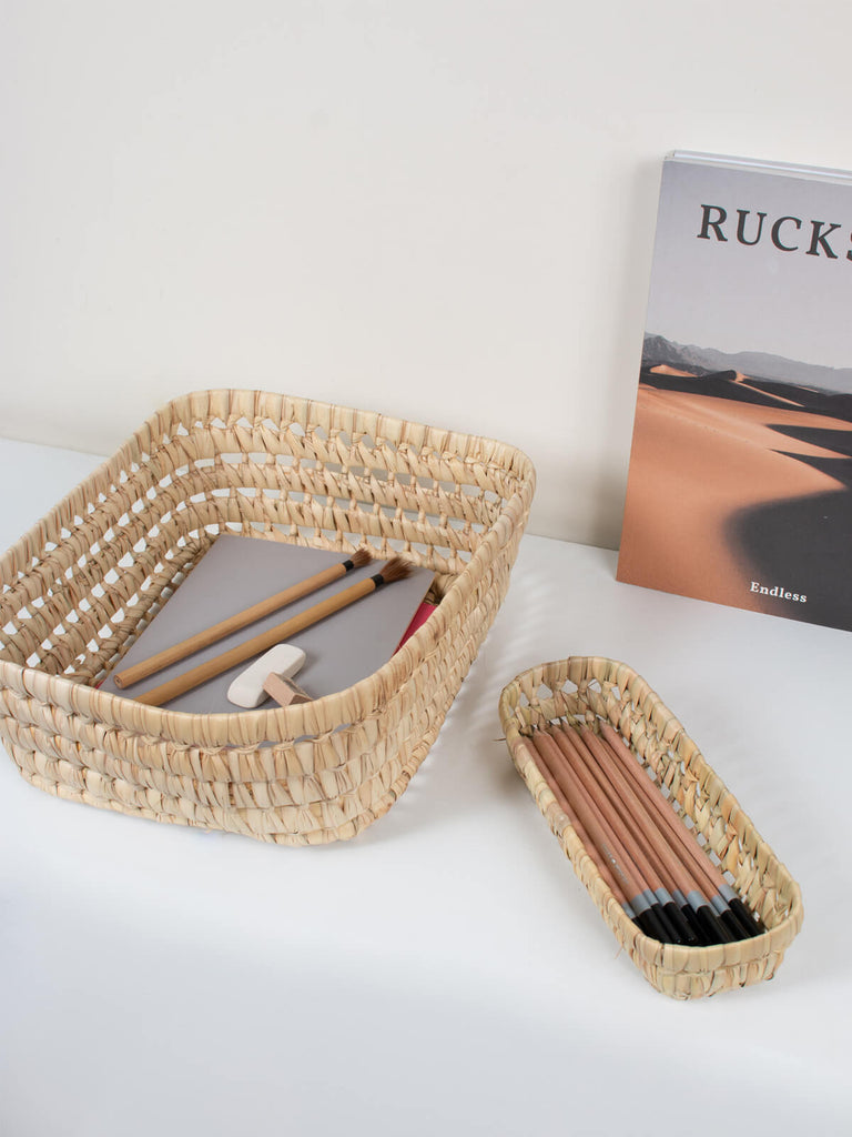 Natural hand woven rectangular storage basket trays with stationery, pens and pencils.
